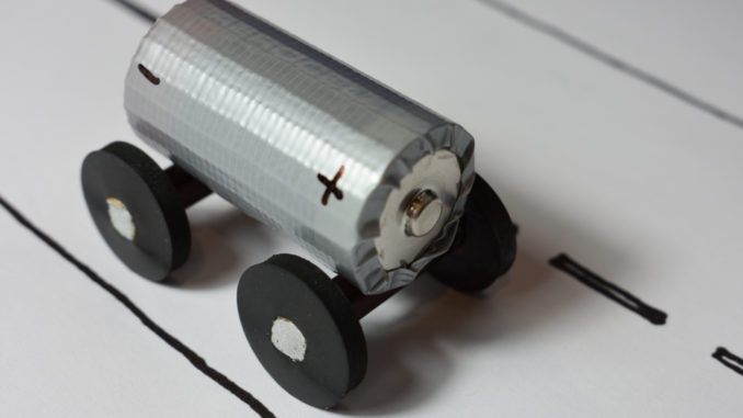 Modell zur Veranschaulichung des Themas Elektromobilität und E-Auto: Eine kleine Batterie auf Gummirädern fährt eine gezeichnete Straße entlang.